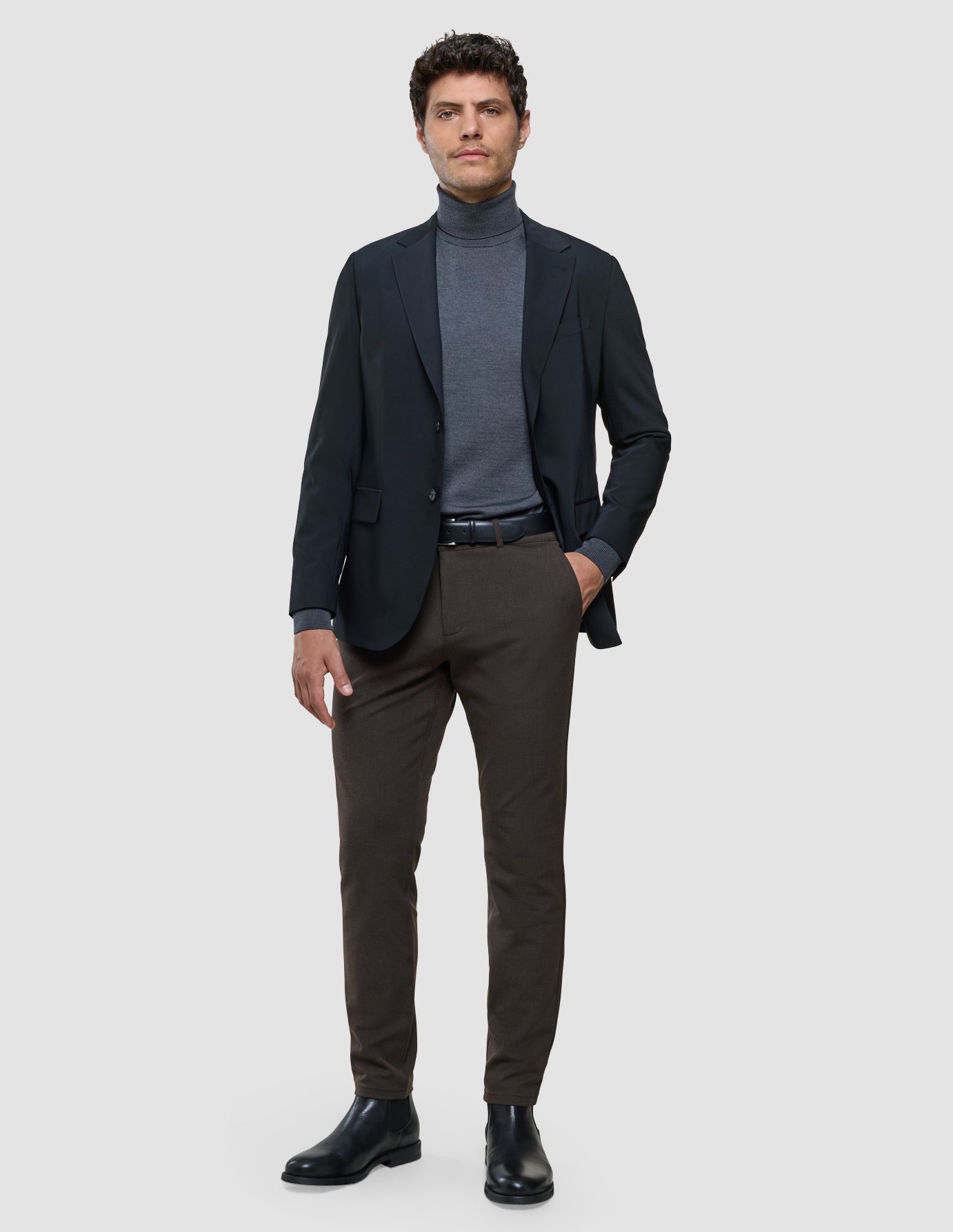 Gen2 Slim i Signature Brown, helfigur af mand iført marineblå blazer, grå rullekravetøj og brune bukser.